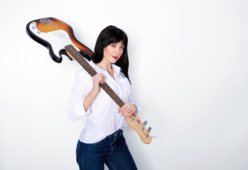 Attractive brunette woman holding her bass guitar on shoulder over gray background