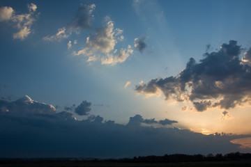 Fototapeta premium The sun setting behind clouds and sunrays above the horizon and colorful sky