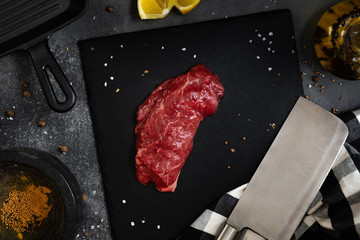 Raw meat, beef butcher or machete steak on black Slate board with Grill pan, knife with spices on a...