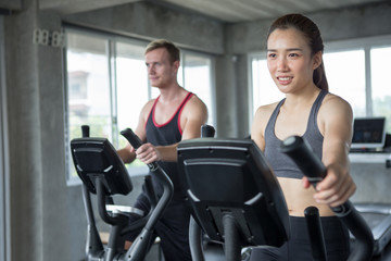 Fototapeta na wymiar Young couple sport exercise with elliptical machine in gym . fitness man and woman workout together ,training,