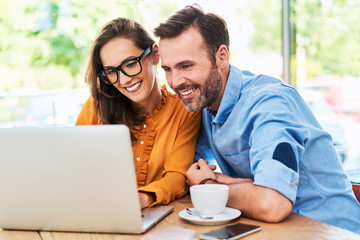 Happy couple using laptop at cafe enjoying time together