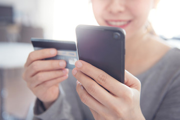 Happy woman shopping online with credit card using smartphone at home.