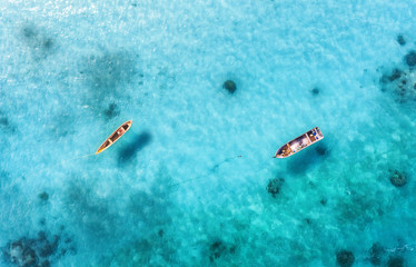 Aerial view of the fishing boats in clear blue water at sunny day in summer. Top view from drone of boat, sandy beach. Indian ocean in Zanzibar, Africa. Landscape with sailboats, clear sea. Seascape