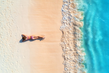 Aerial view of the beautiful young lying woman on the white sandy beach near sea with waves at...