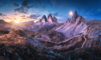 Mountain valley at beautiful sunset. Autumn landscape with mountains, hills, stones, grass, blue sky with clouds and moon at night. High rocks at dusk. Twilight in Tre Cime in Dolomites, Italy. Travel - obrazy, fototapety, plakaty