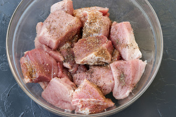 Pork meat cut into large pieces for shish kebab with spices in a transparent bowl