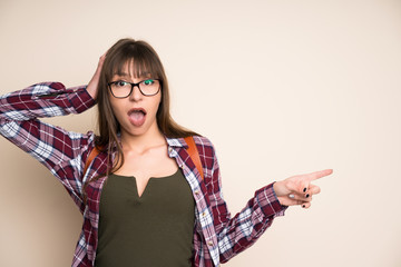 Young woman on ocher background pointing finger to the side and presenting a product