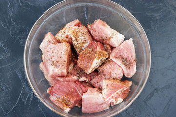 Pork meat cut into large pieces for shish kebab with spices in a transparent bowl