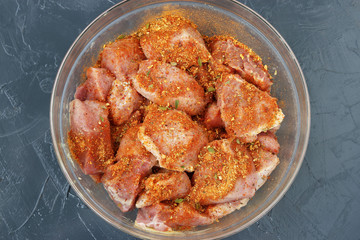 Pork meat cut into large pieces for shish kebab with spices in a transparent bowl