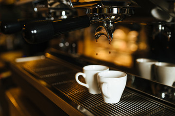 The moment of the brewing process of espresso. Coffee pours into two white cups.