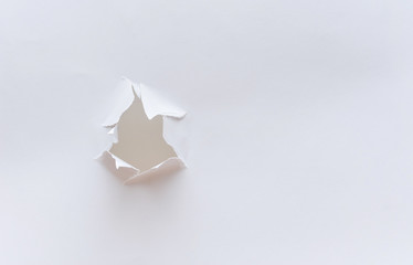 Hole in the paper, on a white background. Accurate shot. Poor quality material. Concept in photography. 