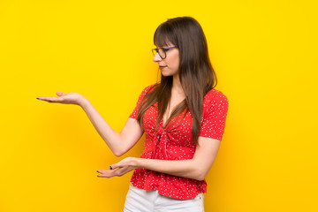 Young woman over yellow wall extending hands to the side for inviting to come