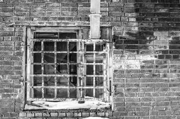 In the photo - a fragment of a wall of red brick, an old window in the wall, covered with rusty bars, covered with old paint, the window overlooks the air vent, a spring Sunny day, close-up, toned.