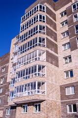 Fototapeta premium The new nine-storey house, illuminated by sunlight, is depicted in a sharp angle from the level of human growth against a clear sky, toned.