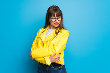 Young woman with yellow jacket on blue background looking down with the hand on the chin © luismolinero