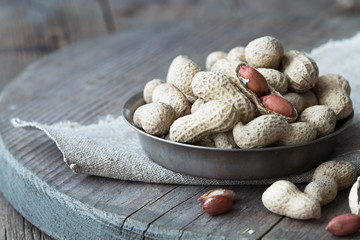 Peanuts in the shell and peeled close up in a cup. Background with peanuts. Roasted peanuts in the shell and peeled on a background of brown cloth in cups