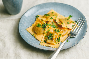 Close-up view of homemade Italian ravioli pasta with parsley on a blue ceramic plate.
