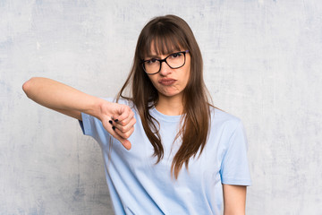 Young woman on grunge background showing thumb down sign