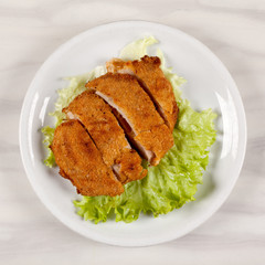 Fried meat cutlet in breadcrumbs sliced and green leaf lettuce.