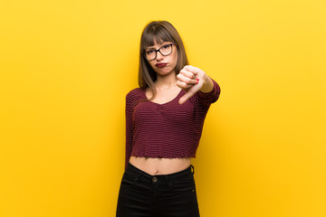 Obraz premium Woman with glasses over yellow wall showing thumb down with negative expression