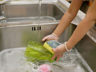 Little baby's hands holding a washing sponge and a green cup, learning to wash it by herself at home - children development through allowing them to do housework