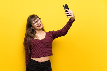 Woman with glasses over yellow wall making a selfie