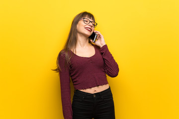 Woman with glasses over yellow wall keeping a conversation with the mobile phone