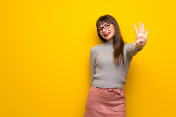 Woman with glasses over yellow wall happy and counting four with fingers