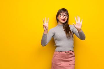 Woman with glasses over yellow wall counting eight with fingers