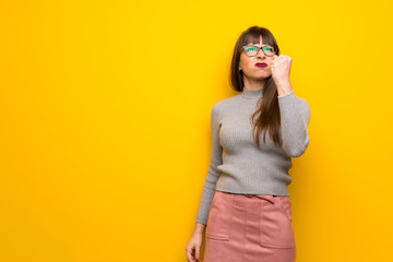 Woman with glasses over yellow wall with angry gesture