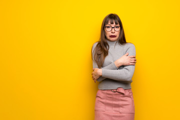 Woman with glasses over yellow wall freezing