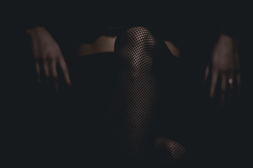slim sexy woman in black stockings sits on a chair on a black background - obrazy, fototapety, plakaty