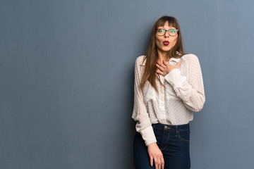Woman with glasses over blue wall with surprise and shocked facial expression