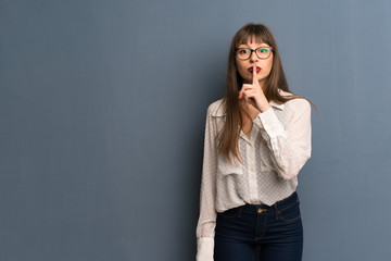 Woman with glasses over blue wall showing a sign of silence gesture putting finger in mouth
