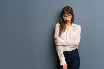 Woman with glasses over blue wall with sad and depressed expression