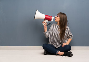 Woman with glasses sitting on the floor shouting through a megaphone