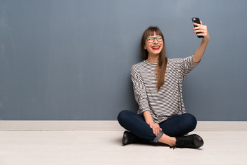 Woman with glasses sitting on the floor making a selfie