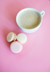 Cup of fresh coffee with macaron on pink background