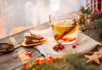 Winter theme. Christmas tea with spices, cup of tea with orange, cinnamon, anise, cookies in a shape of star, pepper and gray scarf on wooden background. Flat lay, View from above. Copy space for text