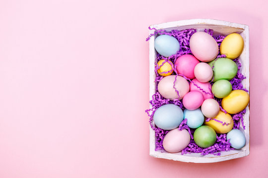 Multicolor eggs in a white tray. Creative Easter concept. Modern solid pink background.