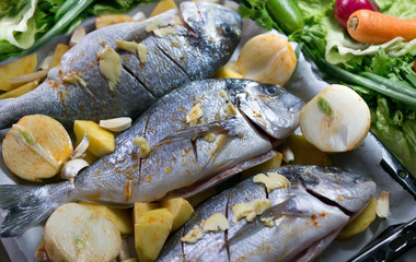 bream fish on a baking tray lined with potatoes and onions