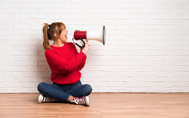 Redhead woman siting on the floor shouting through a megaphone