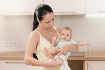 Portrait of beautiful young mother holding her newborn baby in kitchen