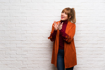 Woman with coat over white brick wall applauding after presentation in a conference