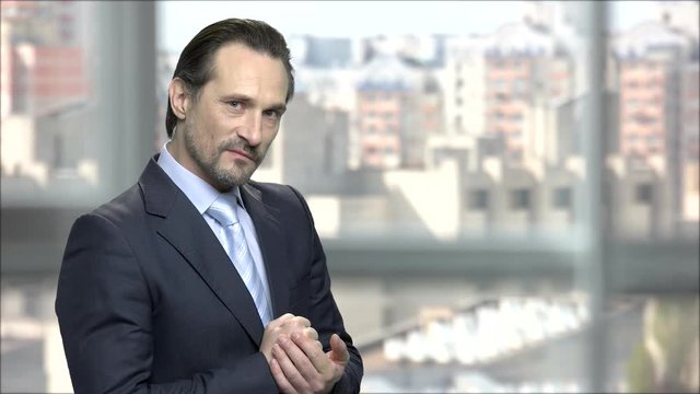 Revengeful mature businessman rubbing his hands. Angry caucasian entrepreneur bethinking plan of revenge. Blur urban city background.