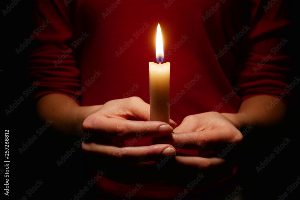 Wall mural Bright candle light in the hands of the girl.  Faith in God.  Prayer with candles in hand.  Woman praying with candles in her hands, close-up.