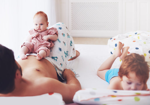 Father Playing With Cute Infant Baby Daughter And Toddler Son In The Morning At Home