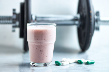 Glass of Protein Shake with milk and raspberries. BCAA amino acids, L - Carnitine capsules and a dumbbell in background. Sport nutrition. Stone / Wooden background. Copy space. 