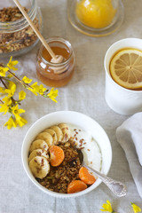 Breakfast of granola with yogurt and tea and forsythia flowers on a linen tablecloth. Rustic style.