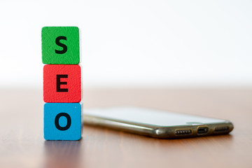 Stacked colorful wooden cubes with the lettering SEO on wooden table beside a mobile phone